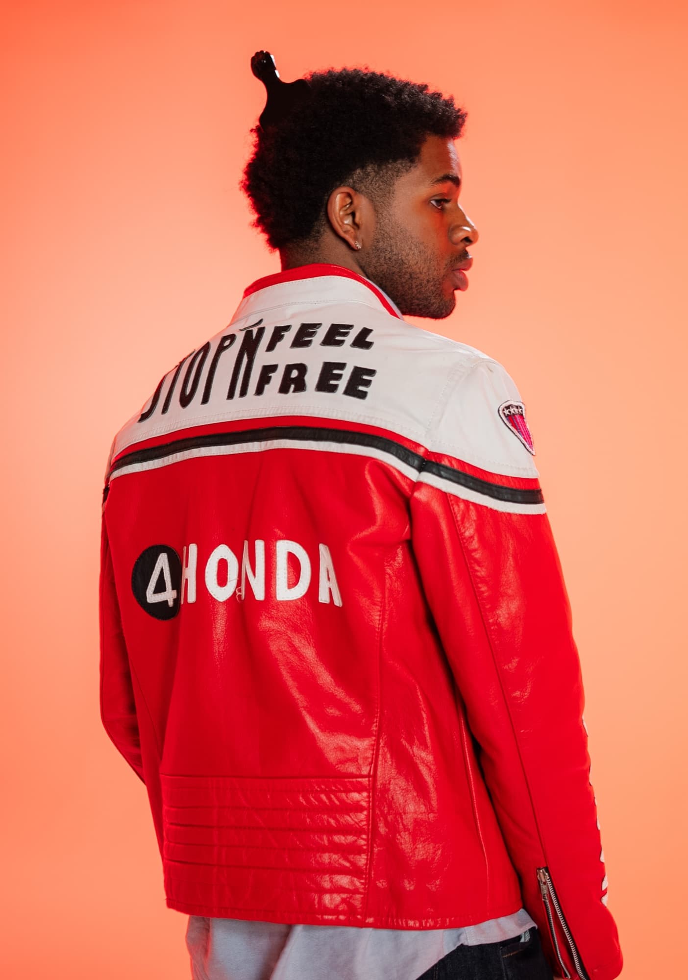 Khari in a red and white Honda racing jacket, looking over his shoulder against a peach backdrop