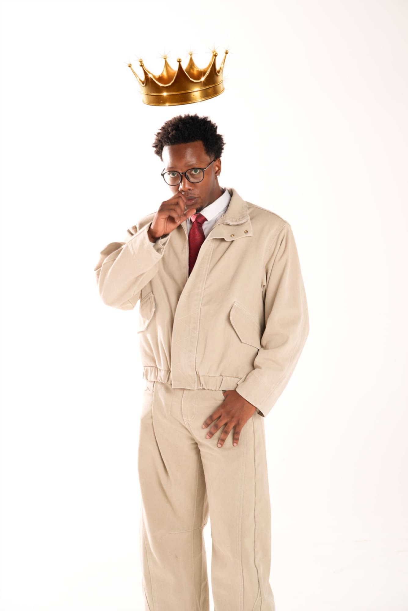 Stevo in a cream workwear suit and red tie with a gold crown floating above his head